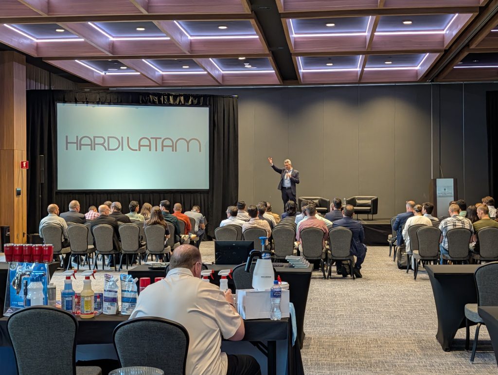 Conferencia HARDI LATAM 2025, con un orador en el escenario frente a una audiencia de profesionales del sector HVAC y la proyección del logo del evento.