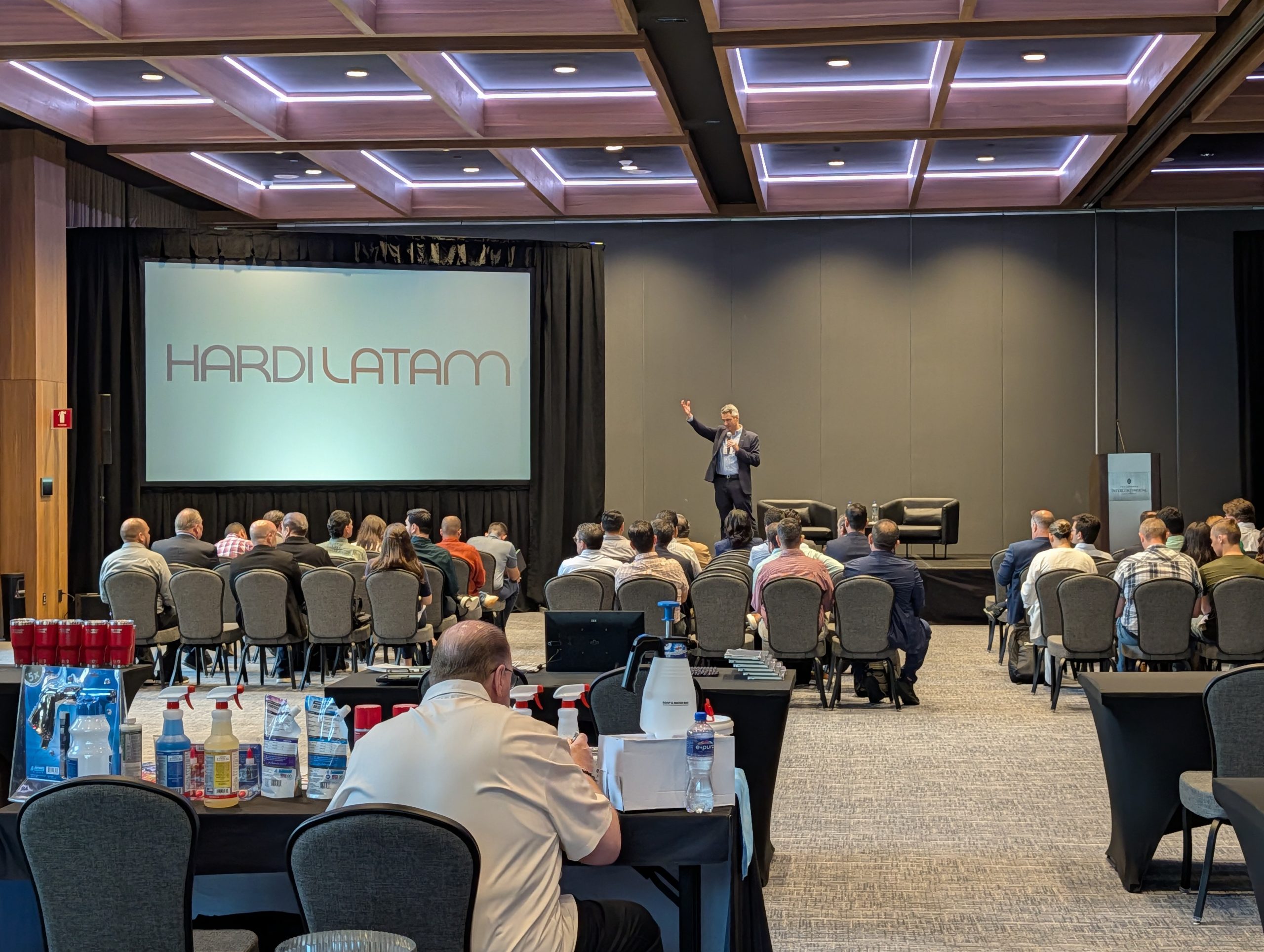 Conferencia HARDI LATAM 2025, con un orador en el escenario frente a una audiencia de profesionales del sector HVAC y la proyección del logo del evento.